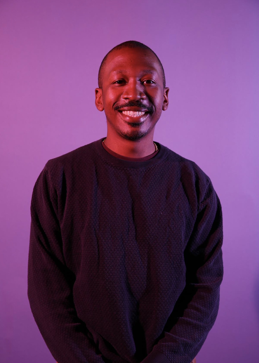 Jordan Chude Williams smiling in a black sweater with a purple background